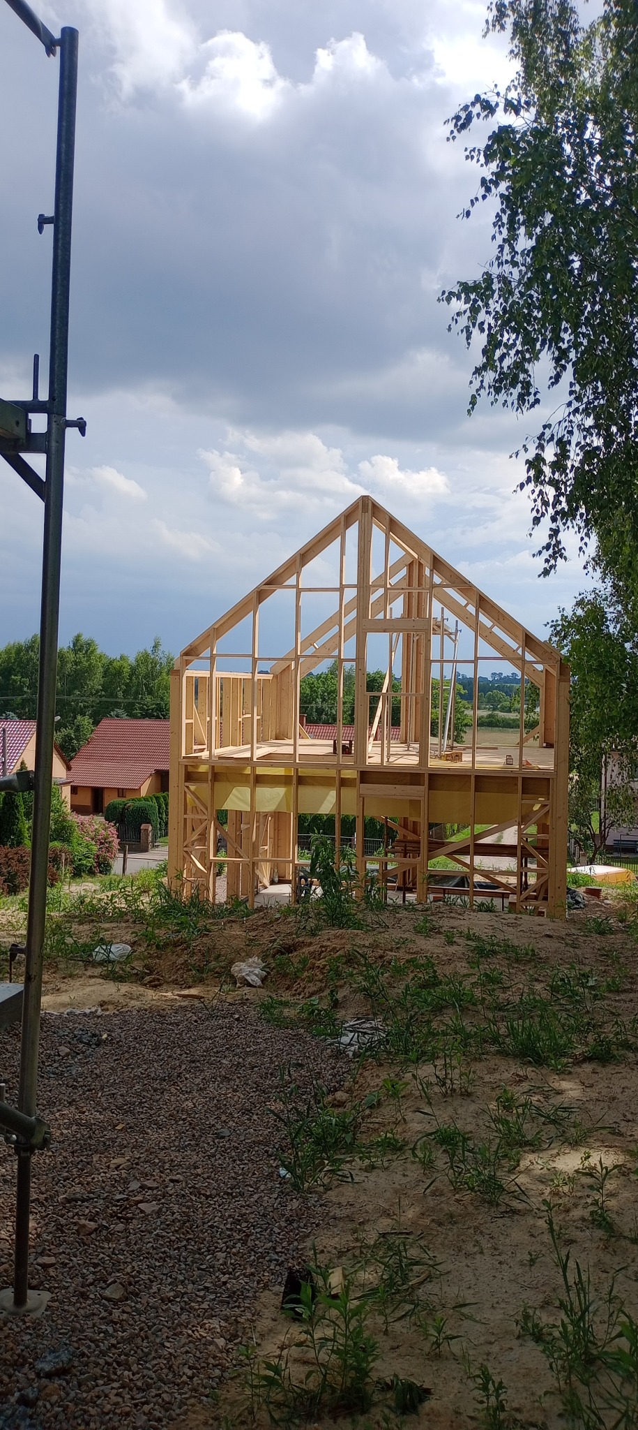 Surowy szkielet dwukondygnacyjnego domu z drewna na tle pochmurnego nieba, widoczny z zewnątrz placu budowy.