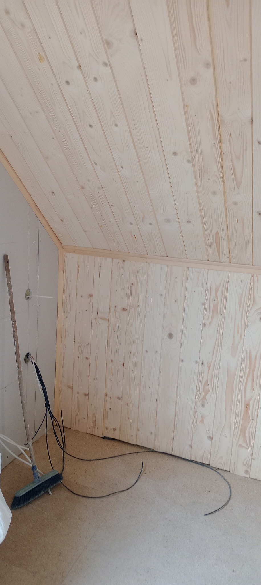 Wykończenie poddasza boazerią z jasnego drewna, widoczne kable i szczotka podczas prac wykończeniowych.