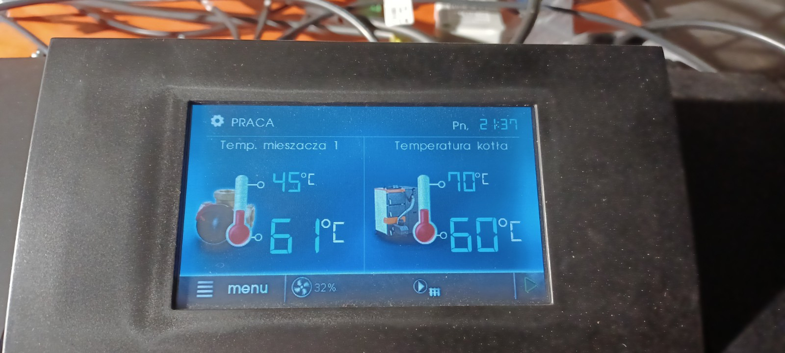 Ekran sterownika kotła grzewczego wyświetlający temperaturę mieszacza i kotła, z widocznymi wartościami 45°C i 70°C oraz 61°C i 60°C, w otoczeniu obudowy z tworzywa sztucznego.