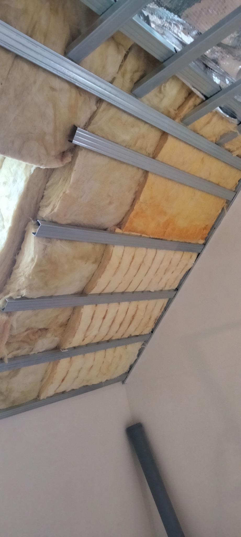 Sufit podwieszany w trakcie montażu: metalowa konstrukcja z widoczną warstwą izolacji z wełny mineralnej, częściowo pokrytą folią aluminiową.