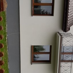 Uslugi - Jasna elewacja budynku z trzema oknami w brązowych ramach i balkonem z ozdobną, metalową balustradą.