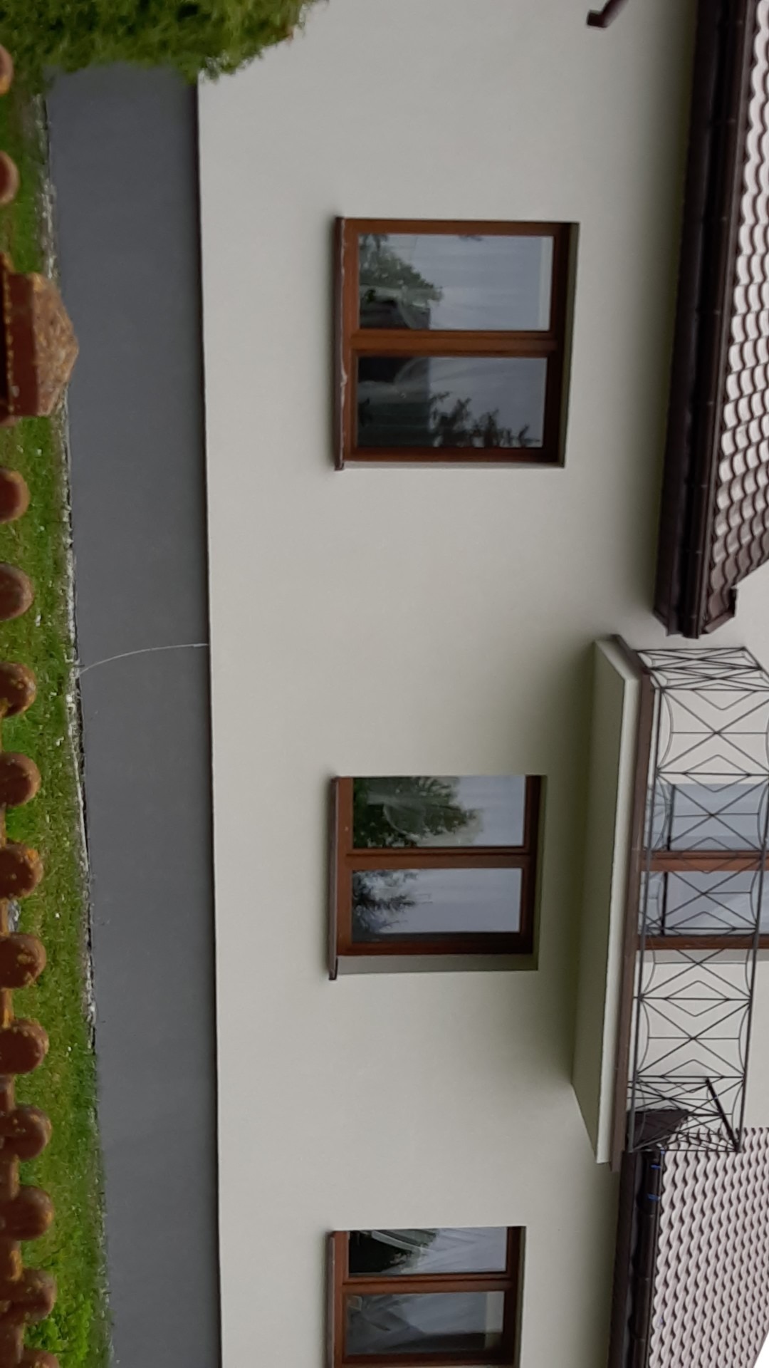 Jasna elewacja budynku z trzema oknami w brązowych ramach i balkonem z ozdobną, metalową balustradą.