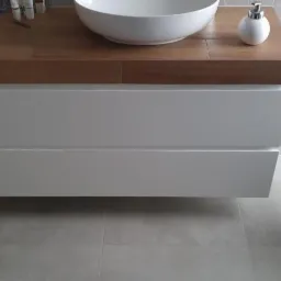 Nowoczesna łazienka z wiszącą szafką pod umywalkę z drewnianym blatem, okrągłą umywalką nablatową i dozownikiem mydła w minimalistycznym stylu, uzupełniona rośliną doniczkową.