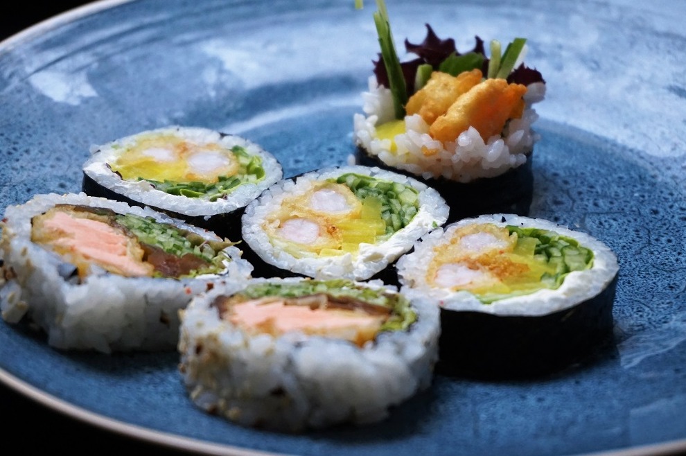 Zestaw sushi z krewetką w tempurze, łososiem i warzywami, ułożony na niebieskim talerzu z efektem spękań.