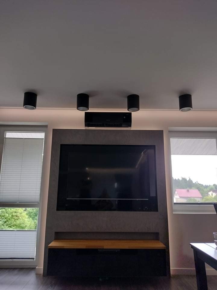Czarny klimatyzator ścienny zamontowany nad telewizorem w salonie z oświetleniem punktowym LED na suficie.