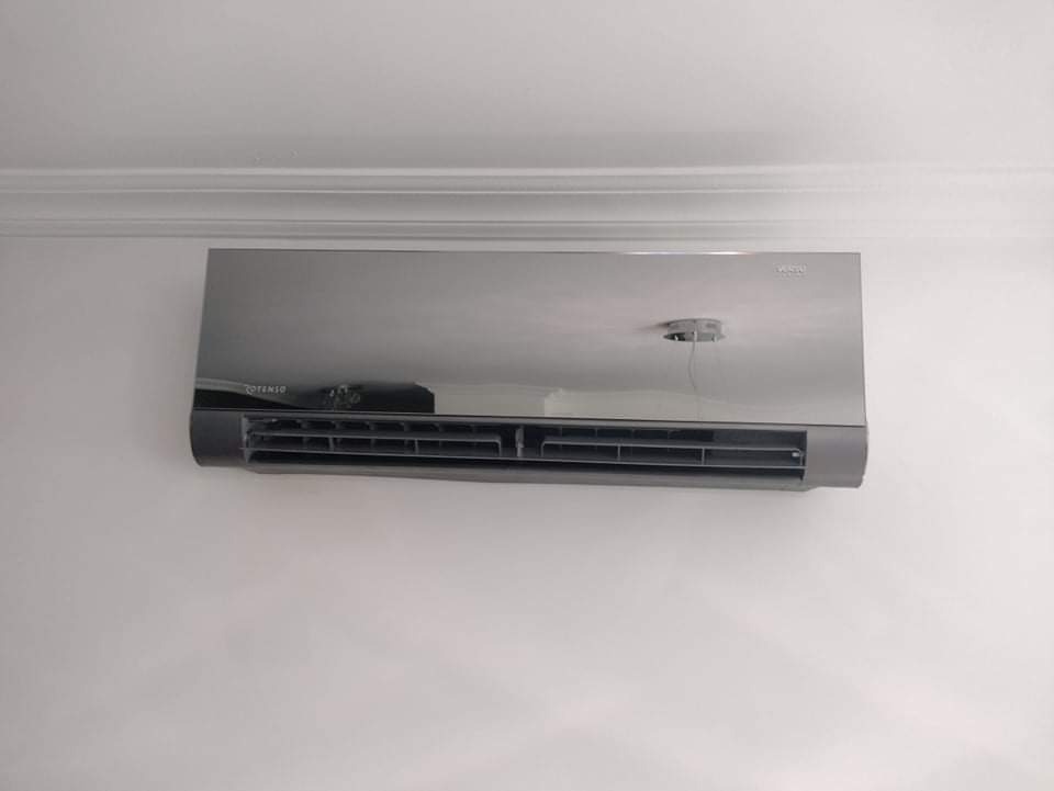 Szary, nowoczesny klimatyzator ścienny marki Rotenso zamontowany w pomieszczeniu z białymi ścianami i sztukaterią sufitową.