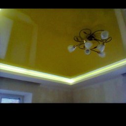 Alfa stroy bud - Żółty, błyszczący sufit z oświetleniem LED po obwodzie i ozdobnym żyrandolem w centralnej części.