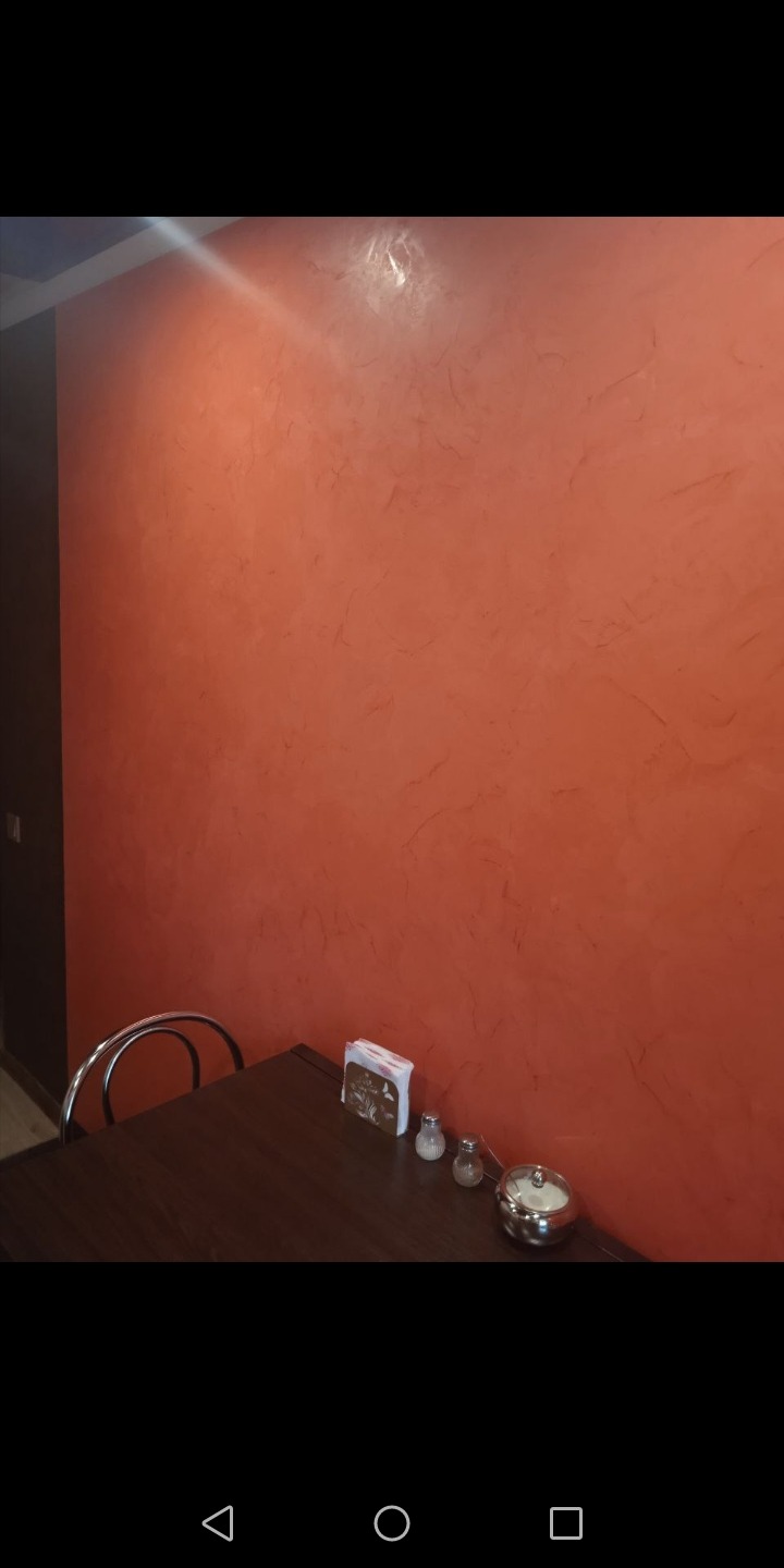 Pomarańczowa ściana z dekoracyjną fakturą w lokalu gastronomicznym, widoczny fragment stołu z przyprawnikami.