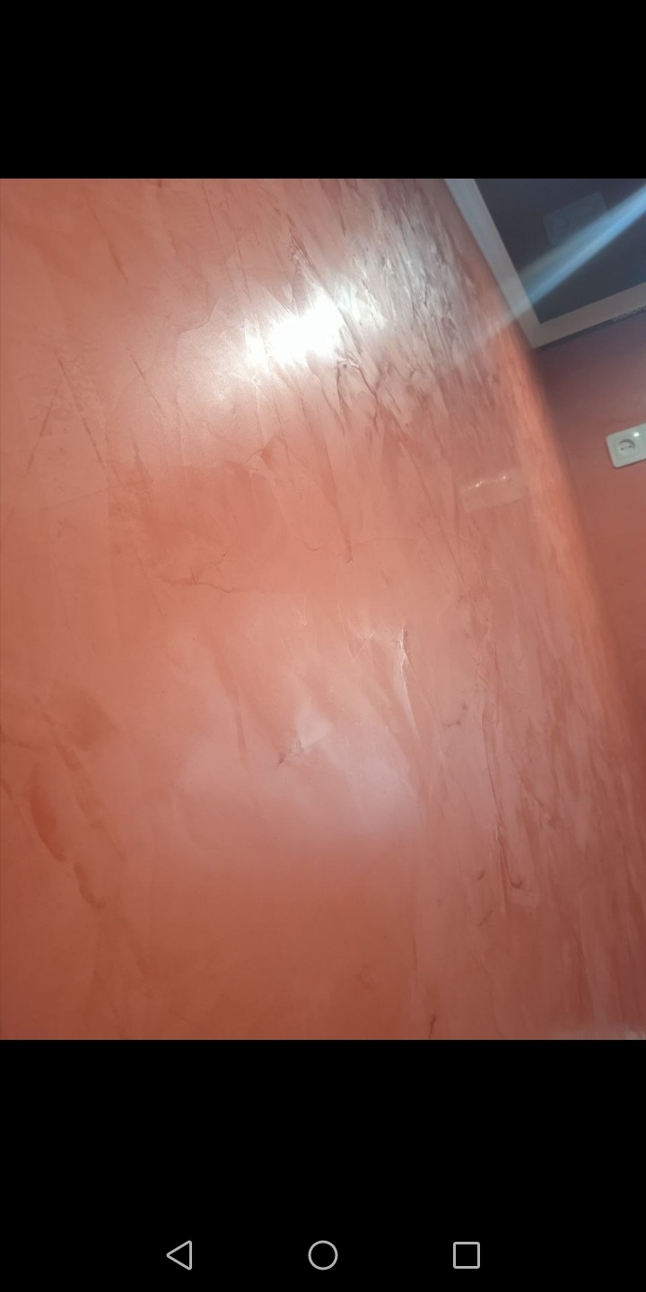 Ściana w odcieniach terakoty z efektem dekoracyjnym przypominającym marmur, widoczne refleksy światła i fragment sufitu z oświetleniem.