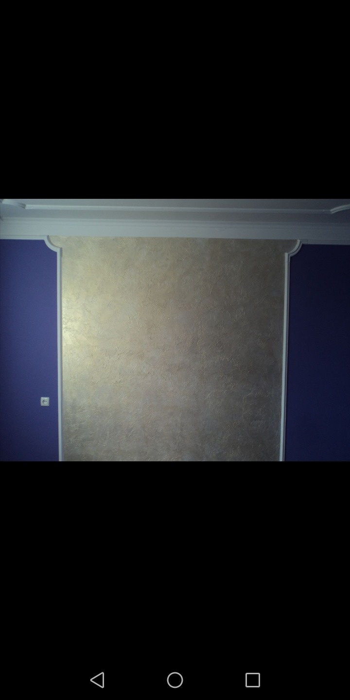 Ściana w pokoju pomalowana na złoto-beżowo z dekoracyjną strukturą, otoczona białą ramą i fragmentem ściany w kolorze ciemnego fioletu.