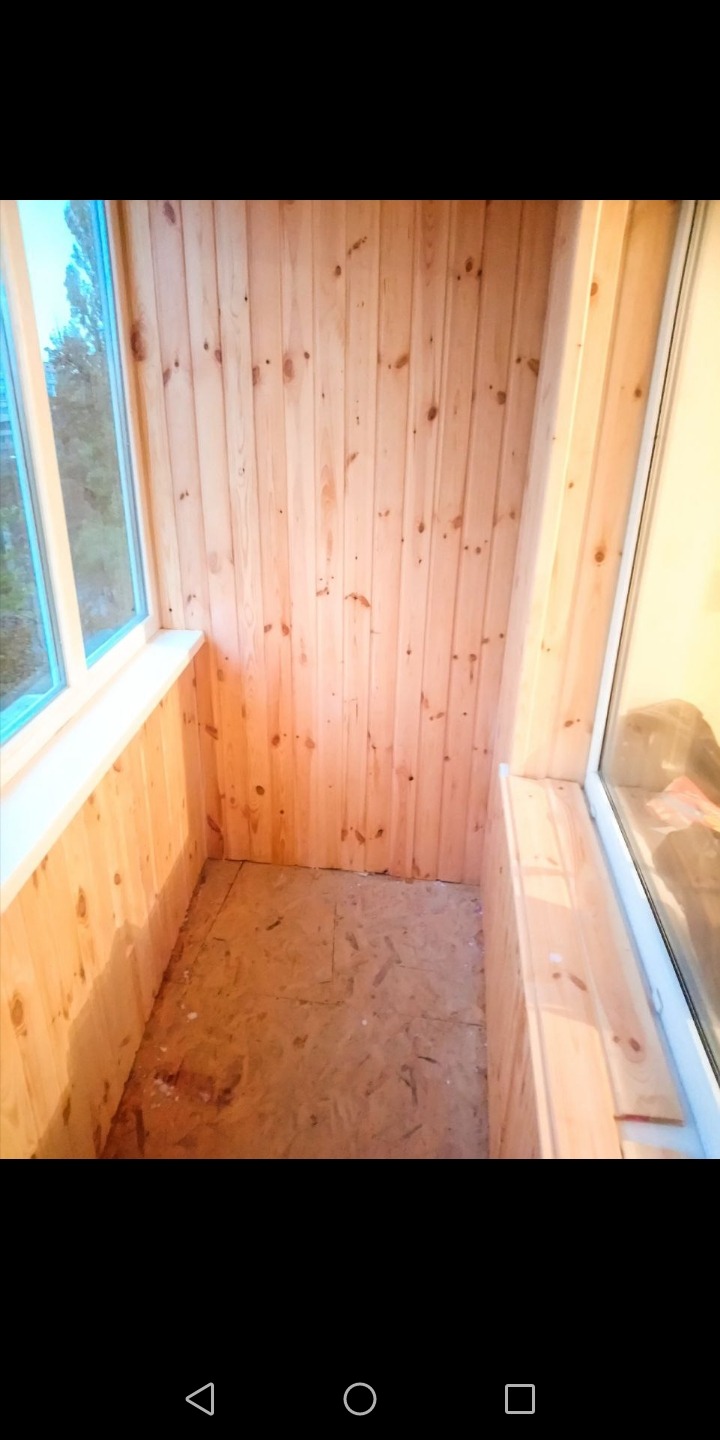 Wykończony balkon z boazerią w jasnym drewnie, widoczne okna z białymi ramami i surowa podłoga z płyty OSB.