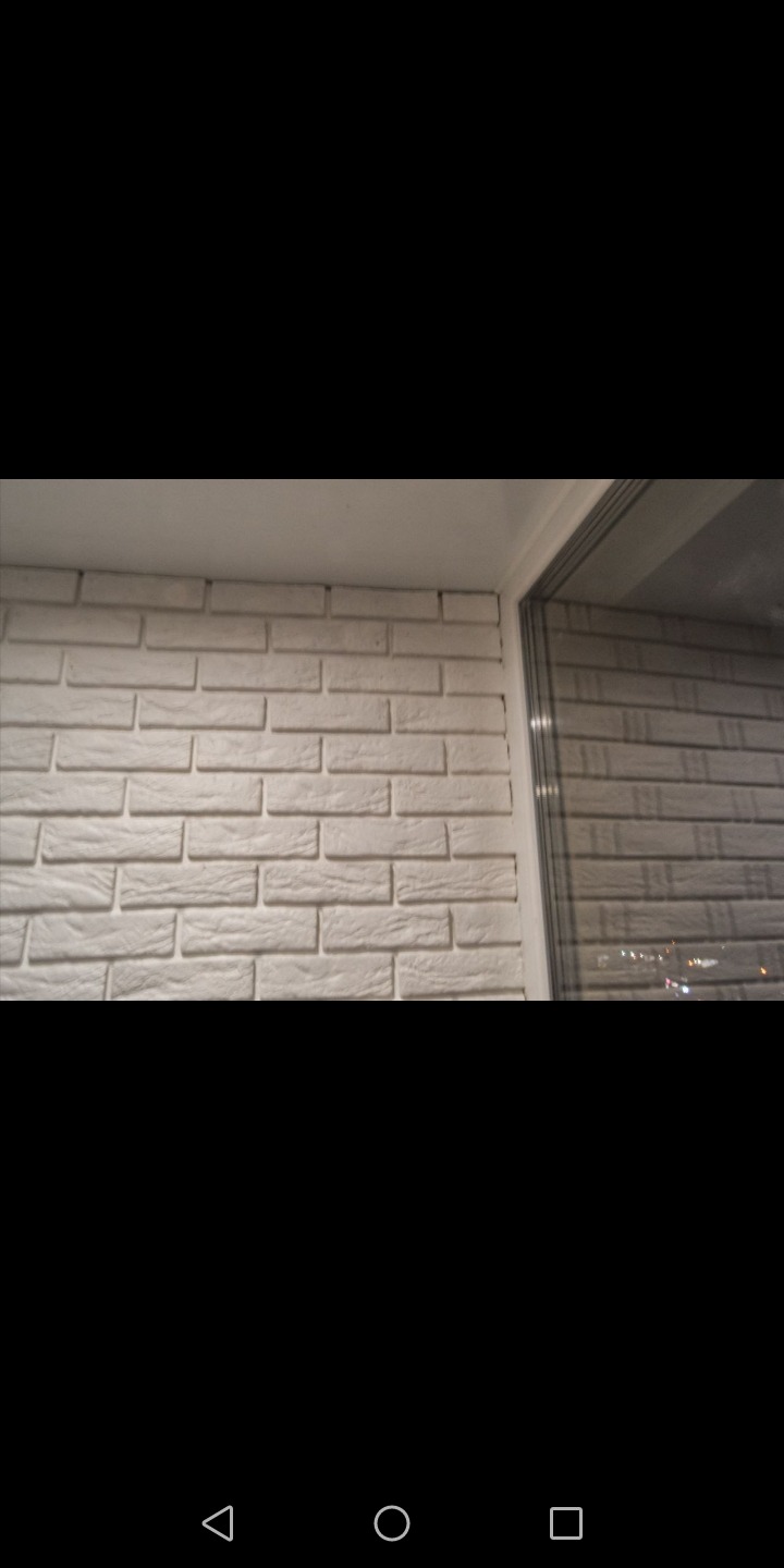 Ściana wykończona białymi płytkami imitującymi cegłę, widoczny narożnik i fragment okna z odbijającym się światłem miasta.