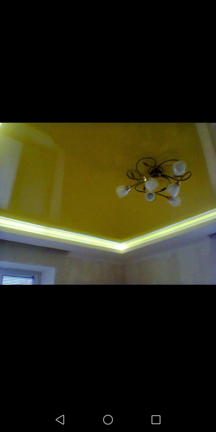 Żółty, błyszczący sufit z oświetleniem LED po obwodzie i ozdobnym żyrandolem w centralnej części.