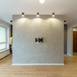 Pusty pokój po remoncie z drewnianą podłogą, ścianą z dekoracyjną fakturą i zamontowanym uchwytem do telewizora.