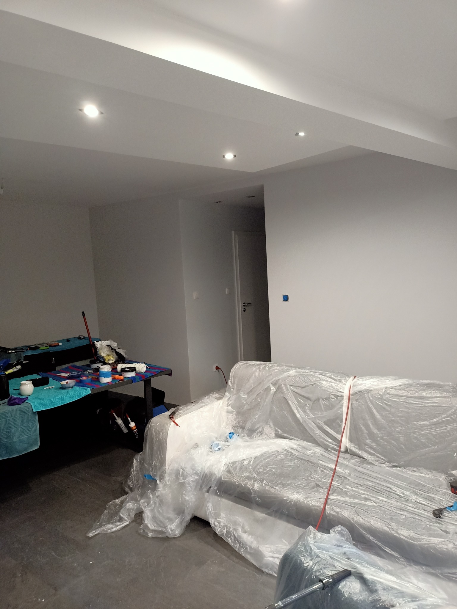 Pokój w trakcie odświeżania ścian, meble zabezpieczone folią malarską, widoczne narzędzia malarskie i akcesoria na stole bilardowym.