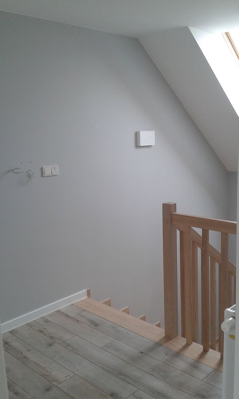 Szare ściany po malowaniu w pokoju na poddaszu ze schodami, widoczne przygotowane stopnie schodów do położenia paneli i drewniana balustrada
