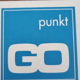 Białe logo 'punkt GO' na błękitnym tle w białej ramce, leżące na drewnianym blacie.