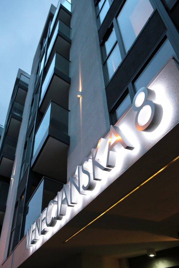 Nowoczesny budynek apartamentowy z balkonami i podświetlanym adresem 'Weneckańska 8', widok z dołu.