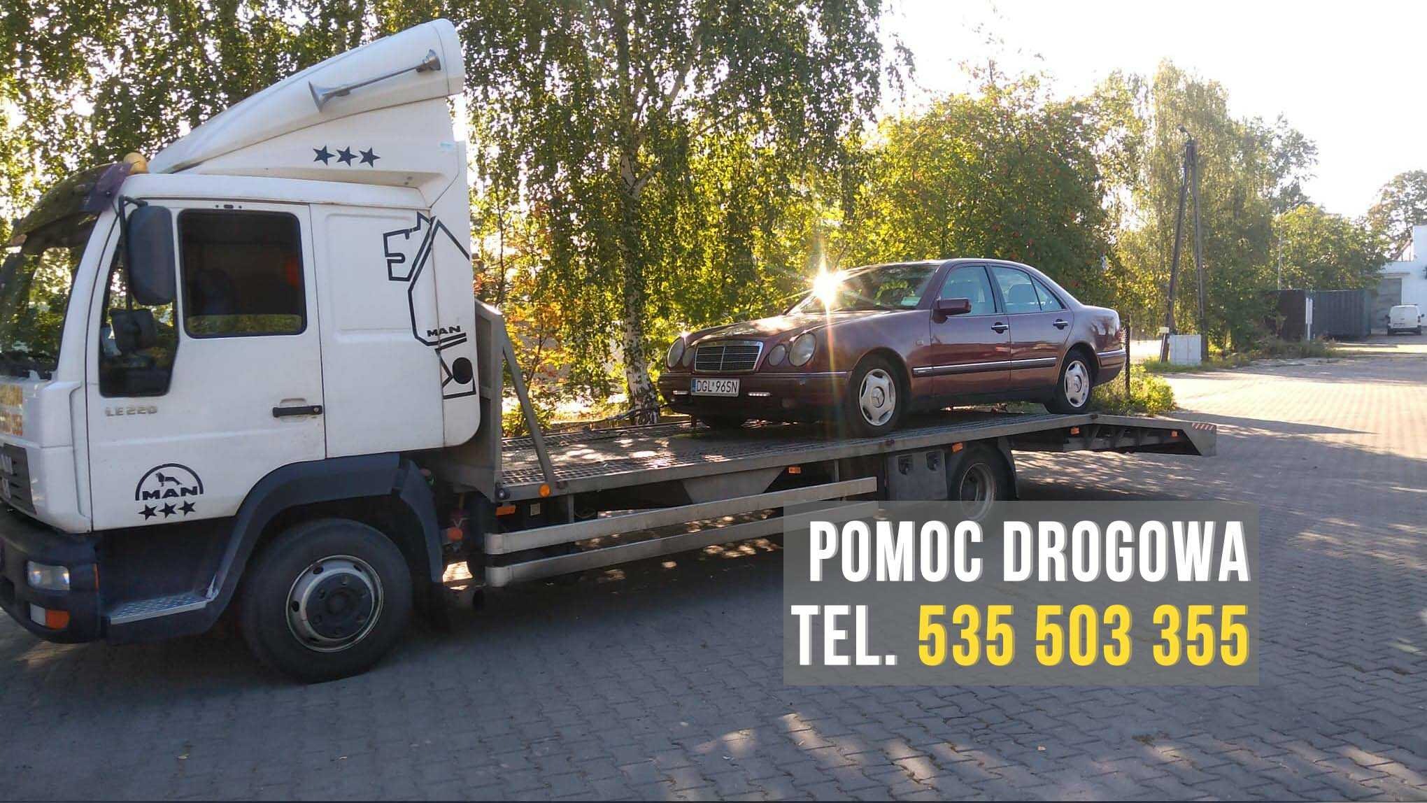 Biała laweta MAN LE 220 z załadowanym, bordowym Mercedesem W210 na tle drzew i budynku, widoczne numery rejestracyjne auta.