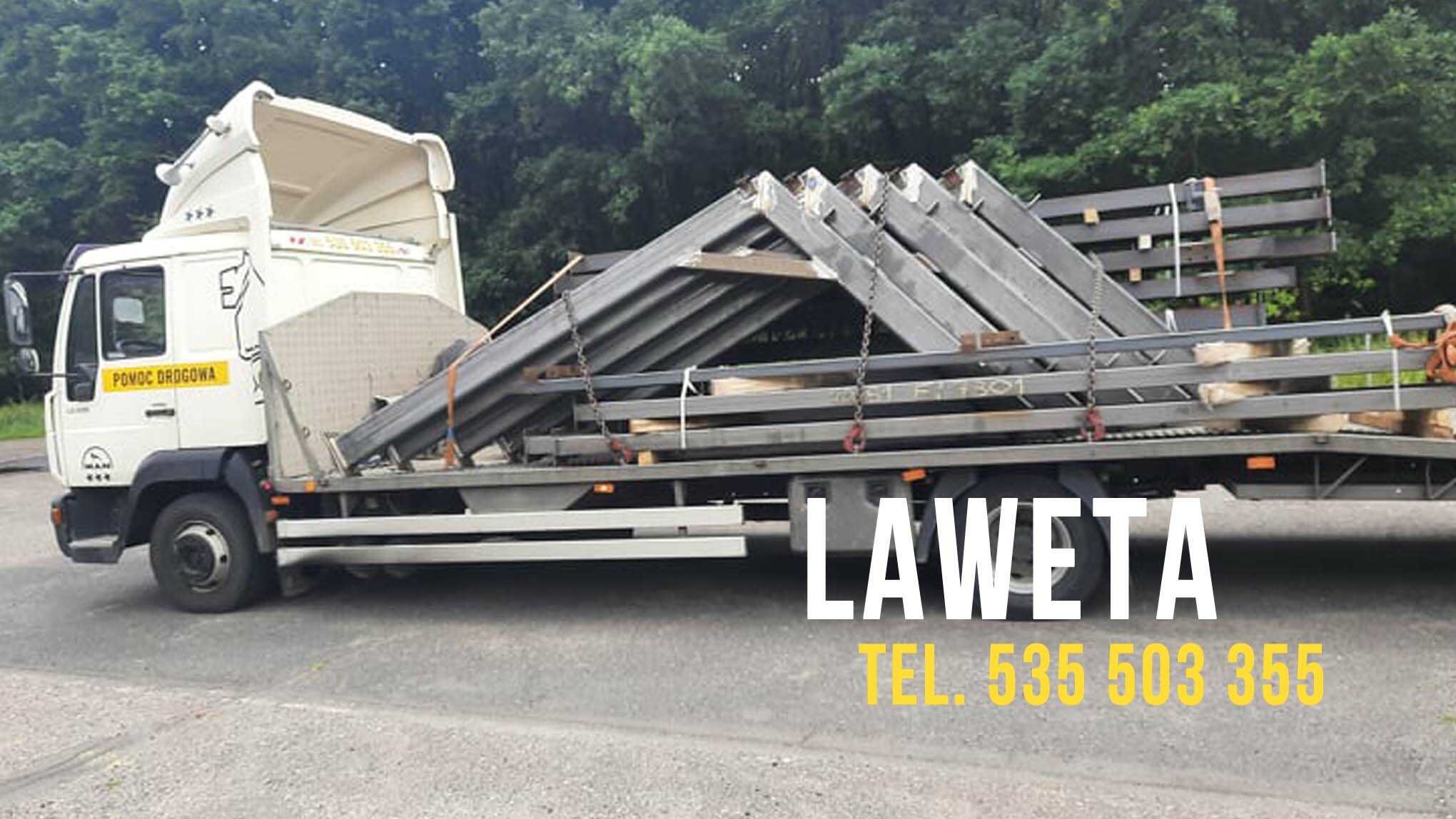 Biała laweta z napisem 'Pomoc Drogowa' przewozi metalowe konstrukcje w kształcie trójkątów, zabezpieczone łańcuchami.