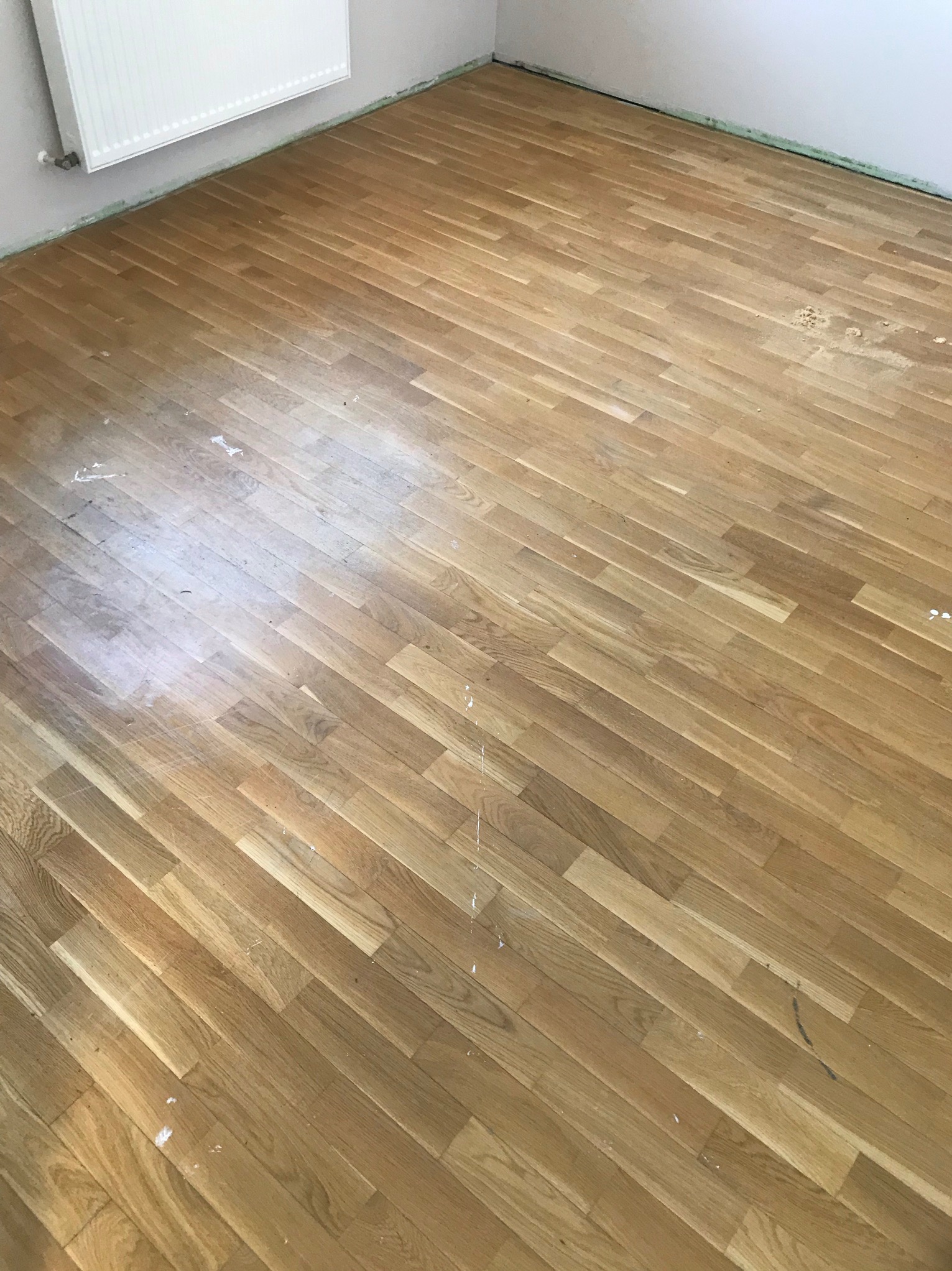 Parkiet po wstępnym szlifowaniu, widoczne ślady po szpachlowaniu i nierównomierny kolor drewna, przygotowany do dalszej obróbki.