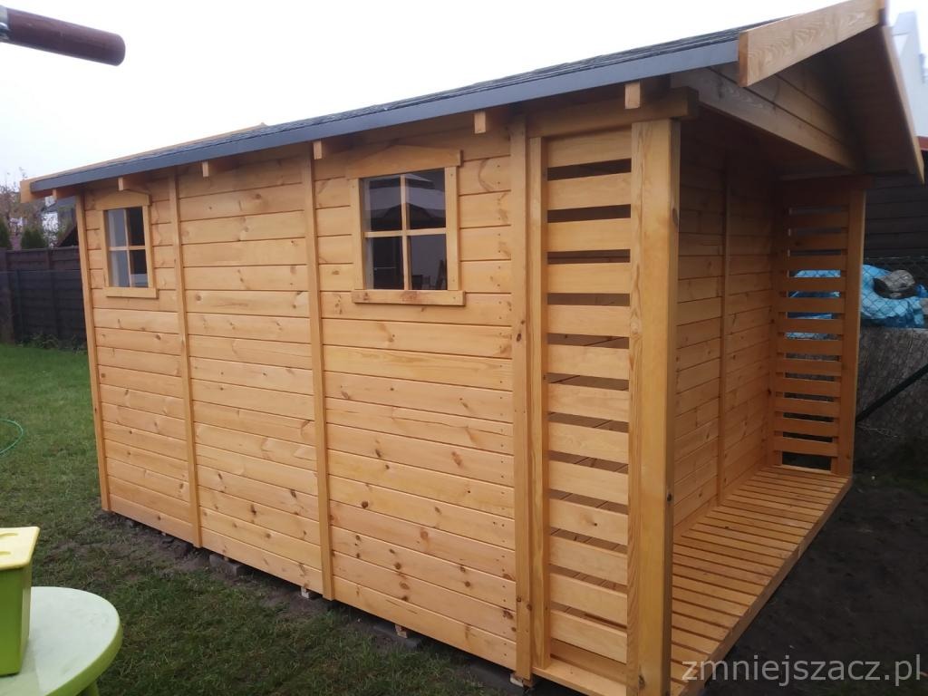 Drewniana altana ogrodowa z dwoma małymi oknami i otwartą przestrzenią z ażurowymi ścianami bocznymi, widoczna na tle trawnika.