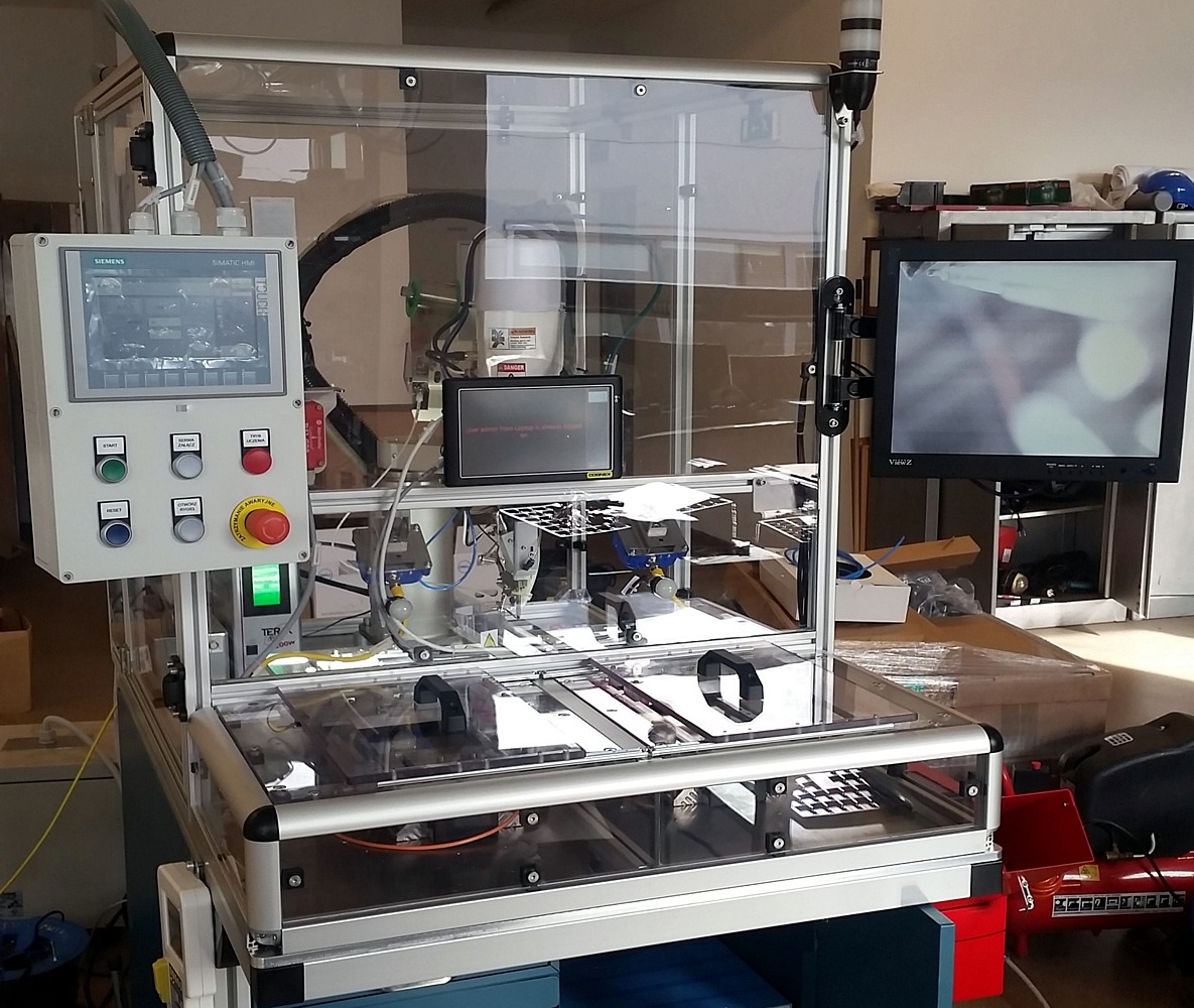 Zautomatyzowane stanowisko pracy z przezroczystą obudową, panelem sterowania Siemens, dwoma monitorami i elementami pneumatycznymi, widoczne elementy bezpieczeństwa.