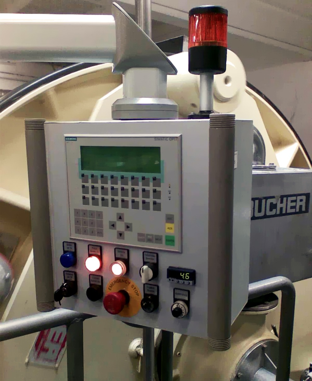 Panel sterowania z przyciskami, wyświetlaczem i lampką ostrzegawczą na tle maszyny przemysłowej, widziany w Warszawie.