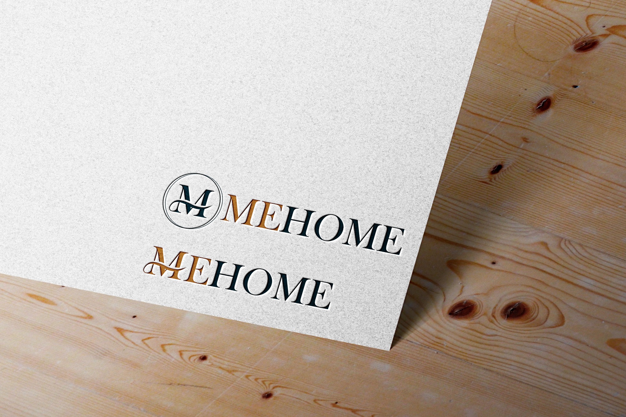 Dwa warianty logo 'MEHOME' na teksturowanym papierze ułożonym na drewnianym blacie. Górny wariant z inicjałem 'M' w okręgu, dolny wariant bez okręgu. Napis w kolorach ciemnozielonym i złotym.