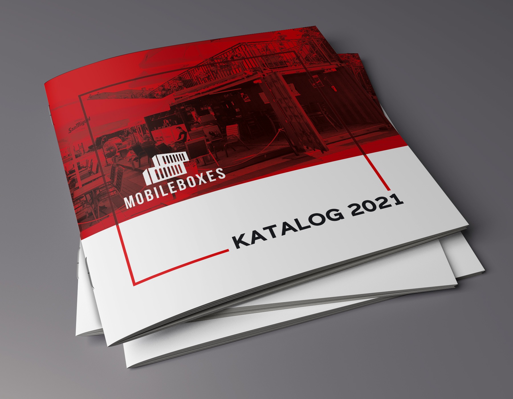 Stos katalogów firmowych z okładką w kolorze czerwonym i białym, prezentujących logo 'MOBILEBOXES' i napis 'KATALOG 2021', leżący na szarym tle.