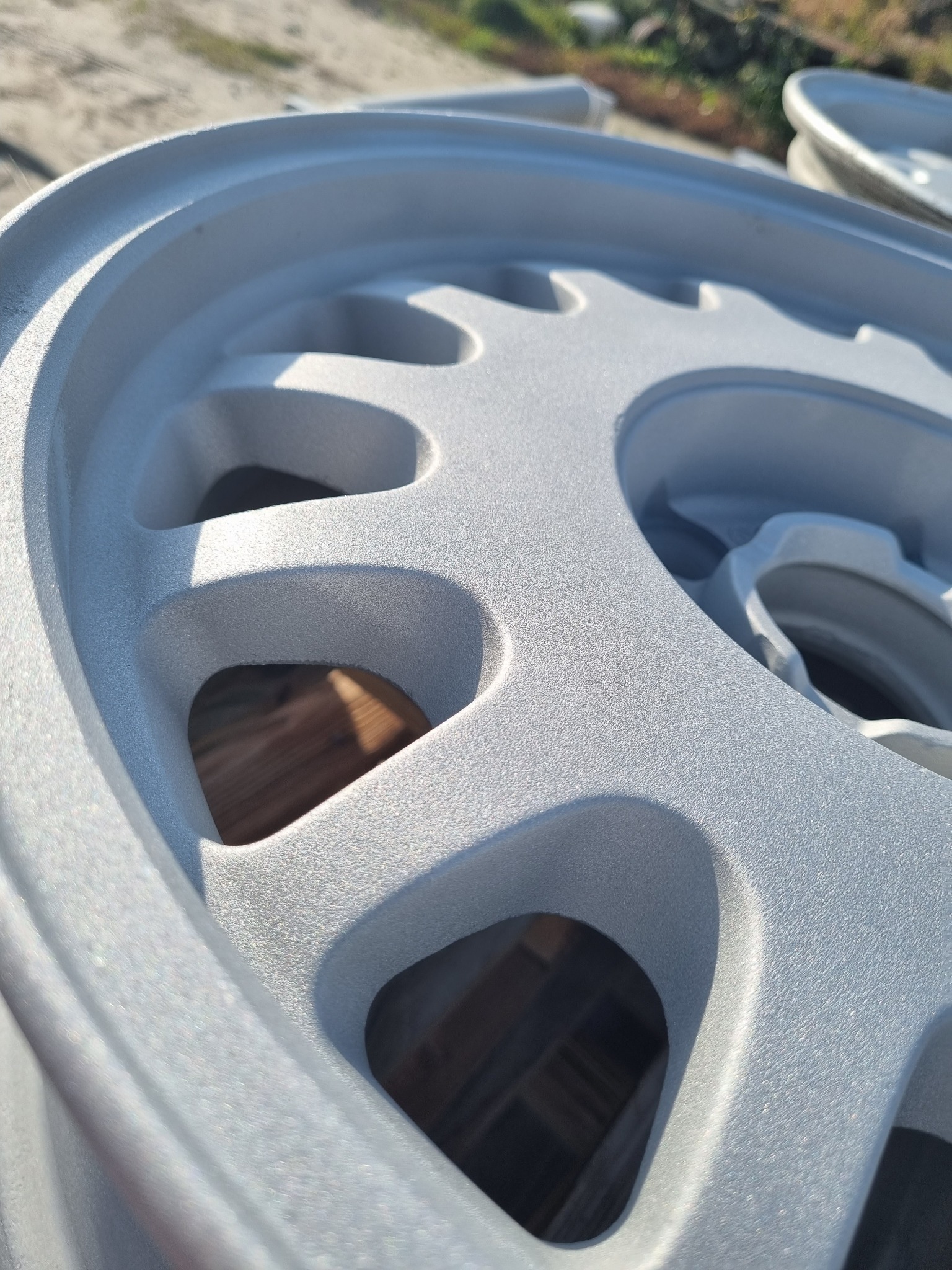 Szczegółowe ujęcie aluminiowej felgi samochodowej po obróbce, pokrytej jednolitą, matową, srebrną powłoką. Widoczne otwory wentylacyjne i delikatna faktura powierzchni.