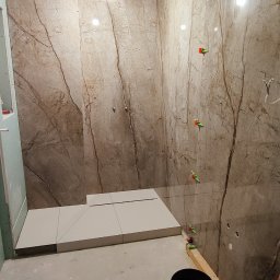 OPTIMUM kompleksowe wykończenia wnętrz - Płytki imitujące marmur na ścianach i podłodze prysznica w trakcie montażu, widoczne poziomice i narzędzia glazurnicze.