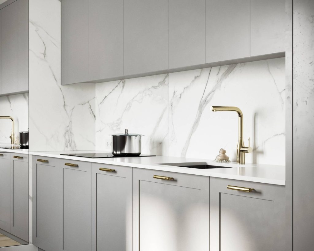 Nowoczesna kuchnia z szarymi szafkami, białym blatem i marmurową ścianą, złota bateria umywalkowa, garnek na płycie indukcyjnej, odbicie w lustrzanej powierzchni