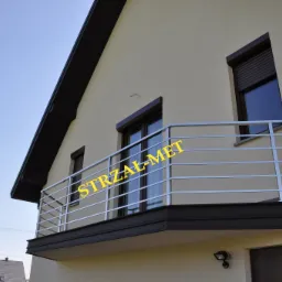 Balkon z nowoczesną, poziomą, metalową barierką, widok z dołu, budynek w jasnych barwach, barierka z prostych, równoległych prętów.