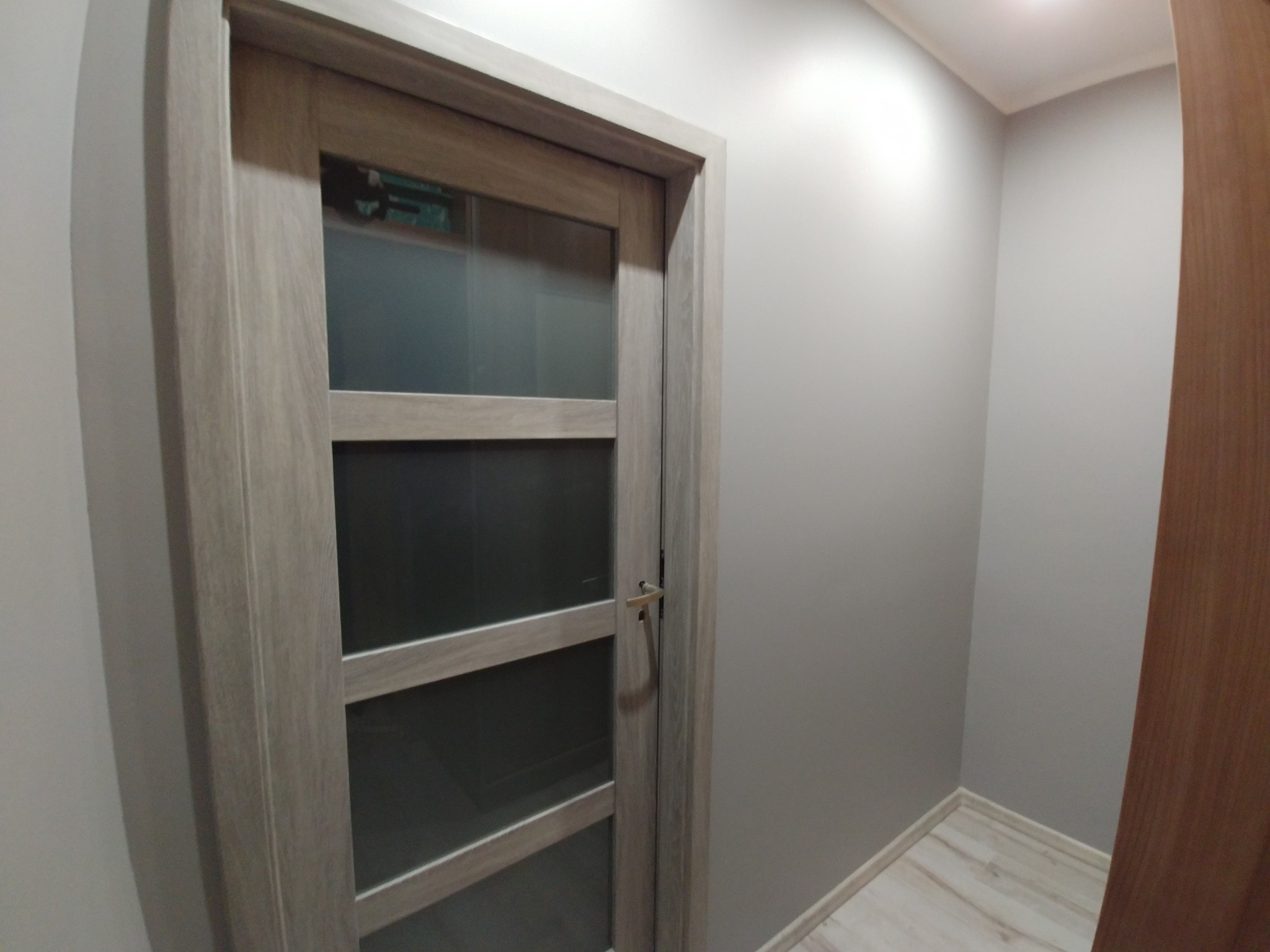 Nowoczesne drzwi wewnętrzne z czterema szybami w drewnianej ramie, zamontowane w szarej ścianie, widoczne z bliska.