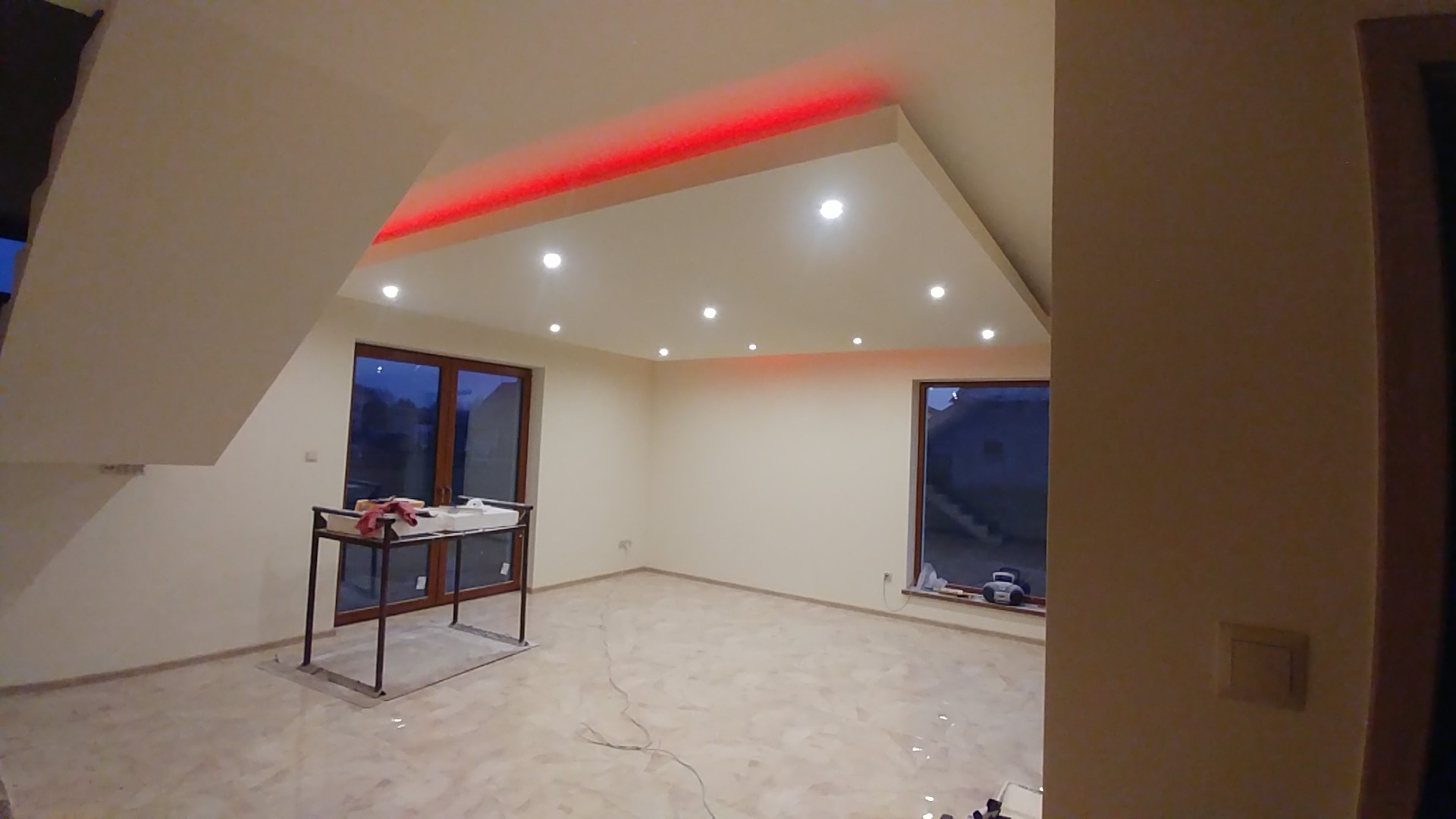 Wnętrze pokoju z podwieszanym sufitem z oświetleniem LED, widoczne okna i stolik z narzędziami malarskimi, podłoga wyłożona płytkami imitującymi marmur.