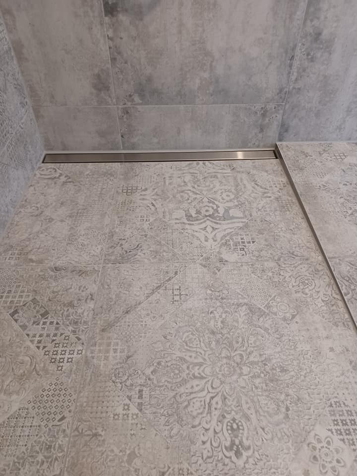 Jasnoszara, wzorzysta podłoga i ściana w łazience z odpływem liniowym w kabinie prysznicowej.