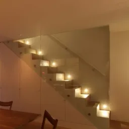 Nowoczesne schody z podświetlanymi stopniami i szklaną balustradą, w tle białe szafki w zabudowie.