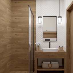 Brucka Studio - Nowoczesna łazienka z drewnianymi panelami ściennymi i podłogą, kabiną prysznicową ze szklanymi drzwiami, umywalką nablatową na drewnianej szafce z koszem na ręczniki, lustrem w czarnej ramie...