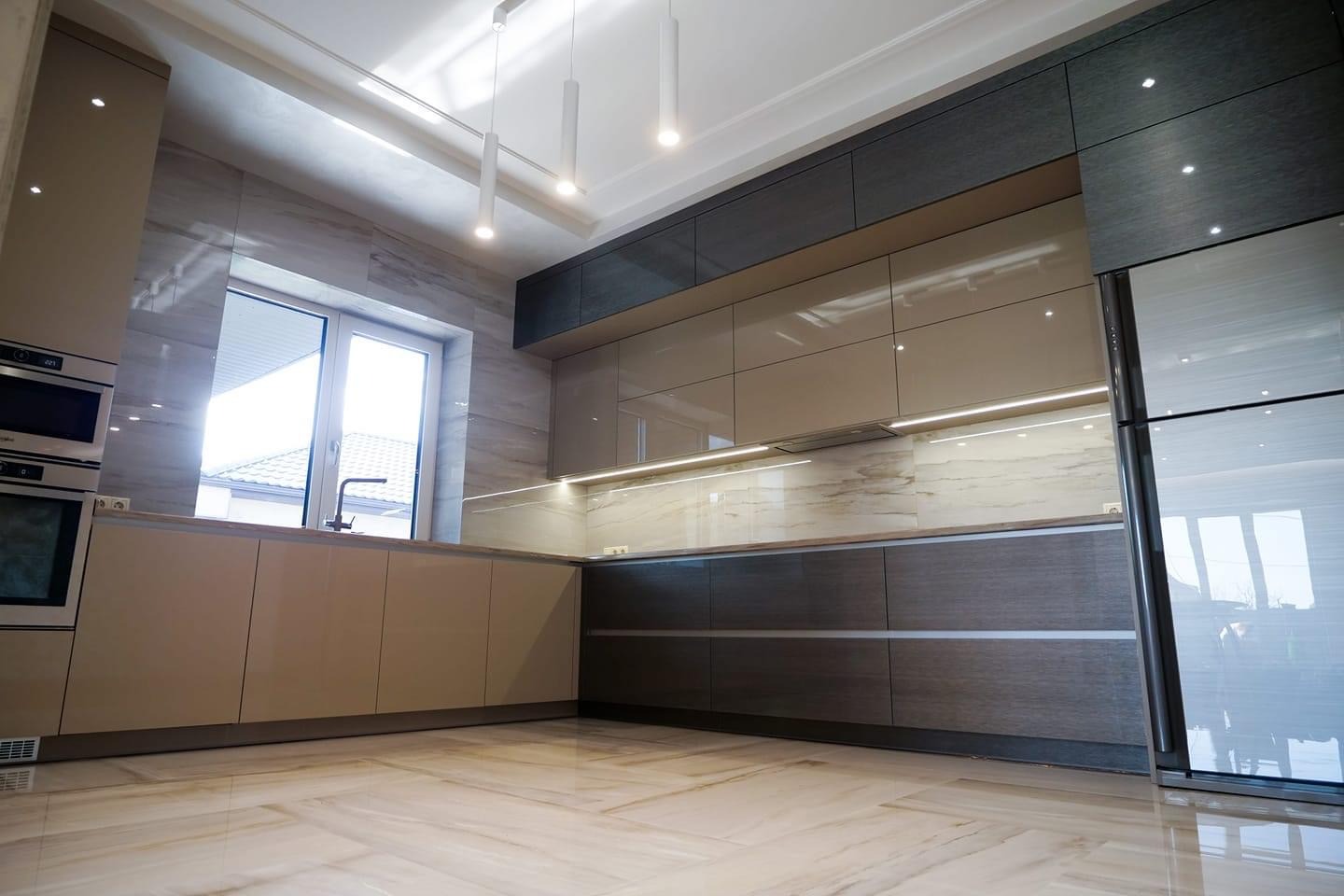 Nowoczesna kuchnia z beżowo-szarymi szafkami z połyskiem, marmurowym blatem i podświetleniem LED, widok z niskiego kąta na podłogę z płytek imitujących marmur.