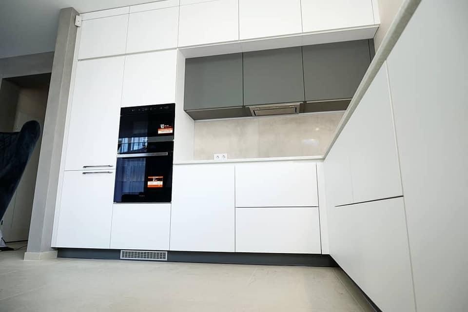 Nowoczesna zabudowa kuchenna z białymi frontami, grafitowymi szafkami wiszącymi i wbudowanym piekarnikiem z wyświetlaczem.