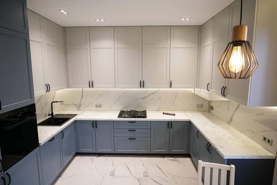 Nowoczesna kuchnia w kształcie litery U z szarymi dolnymi szafkami i białymi górnymi, blatem i backsplashiem z białego marmuru, czarnym zlewozmywakiem i baterią oraz designerską lampą wiszącą.