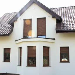 Biały dom jednorodzinny z brązowymi roletami zewnętrznymi opuszczonymi na wszystkich oknach, widok z zewnątrz w słoneczny dzień.