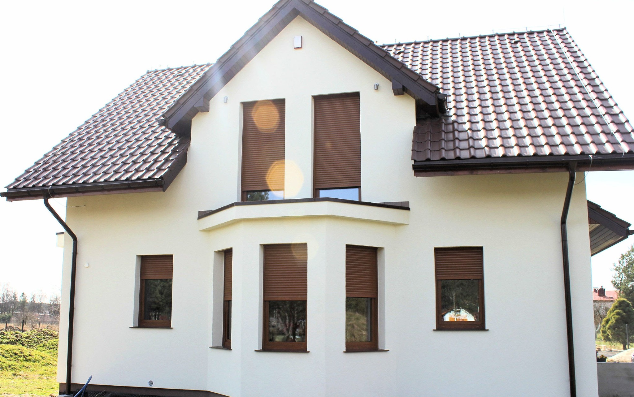 Biały dom jednorodzinny z brązowymi roletami zewnętrznymi opuszczonymi na wszystkich oknach, widok z zewnątrz w słoneczny dzień.