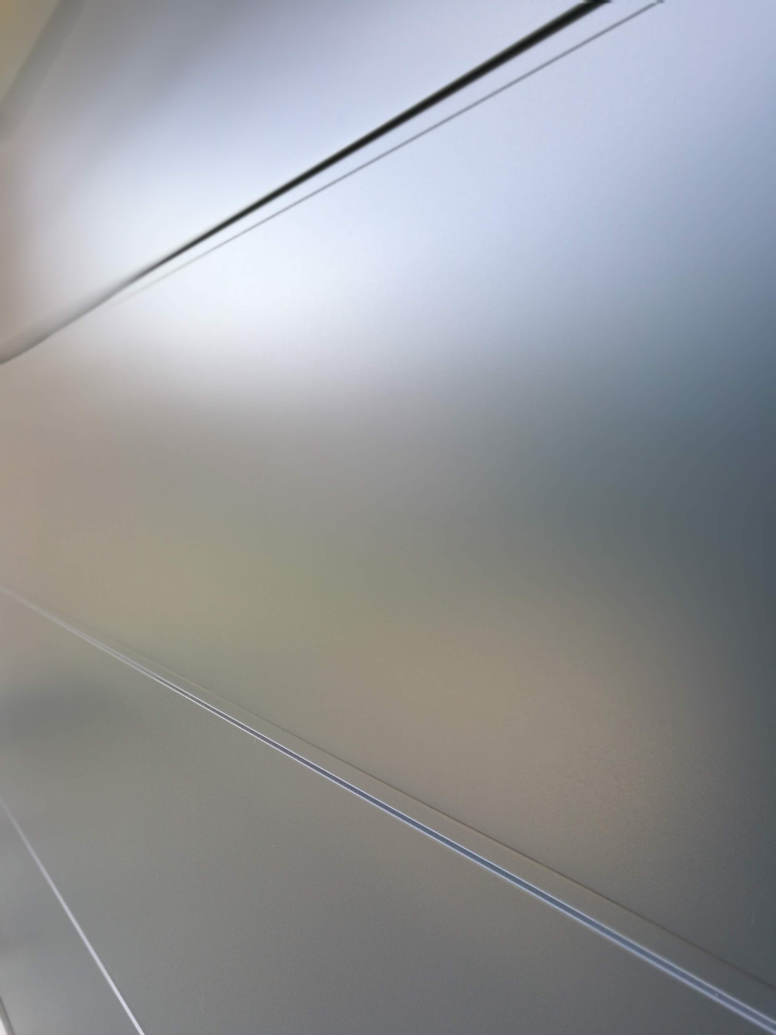 Fragment szarej, metalowej bramy garażowej z widocznymi poziomymi przetłoczeniami i delikatną fakturą powierzchni, sfotografowanej pod kątem.