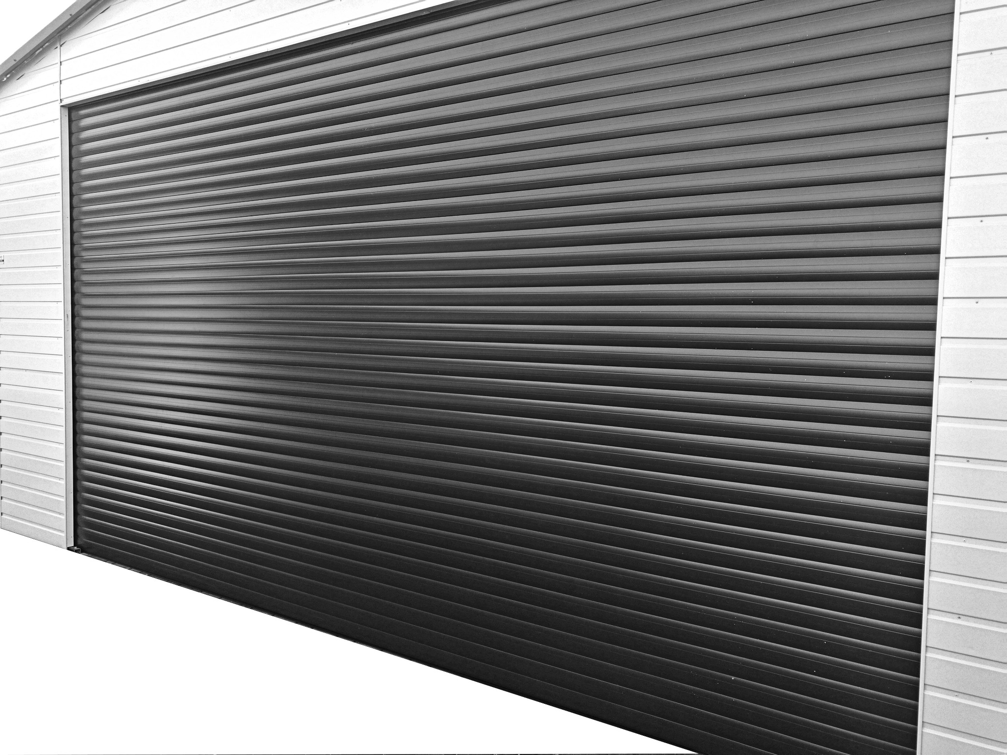 Zamknięta, pozioma, grafitowa brama garażowa rolowana z widoczną strukturą paneli, zamontowana w białej elewacji budynku.