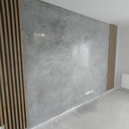 BOBI MAKER USŁUGI BUDOWLANE - Ściana wykończona w stylu betonu architektonicznego z dekoracyjnymi panelami lamelowymi po bokach, widoczna instalacja elektryczna.