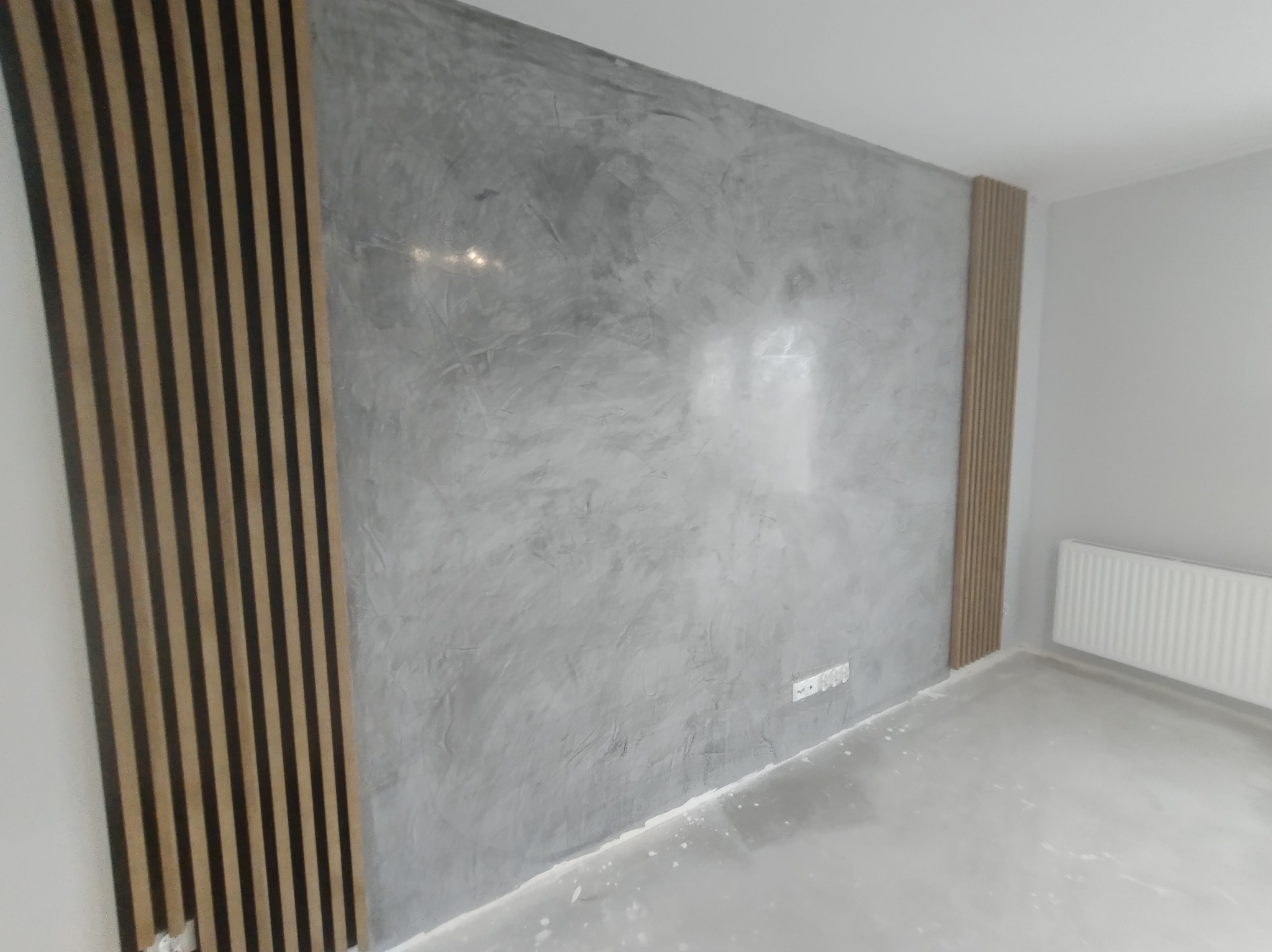 Ściana wykończona w stylu betonu architektonicznego z dekoracyjnymi panelami lamelowymi po bokach, widoczna instalacja elektryczna.