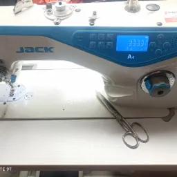 Przemysłowa maszyna do szycia marki Jack A4 z wyświetlaczem cyfrowym, nożyczkami obok i naklejką informacyjną Majster na obudowie.