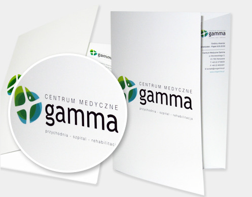Biała teczka firmowa z logo Centrum Medycznego Gamma, widoczna z bliska w powiększeniu, obok teczka otwarta z danymi adresowymi i kontaktowymi firmy.